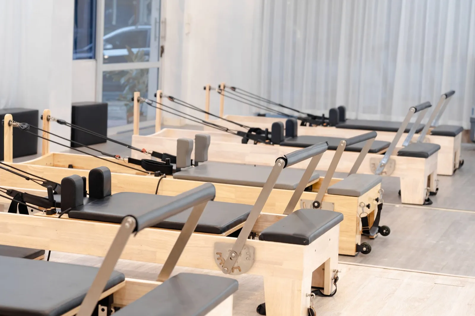 Salle claire avec reformer et tapis, deux personnes suivant un cours de Pilates près d'une baie vitrée.
